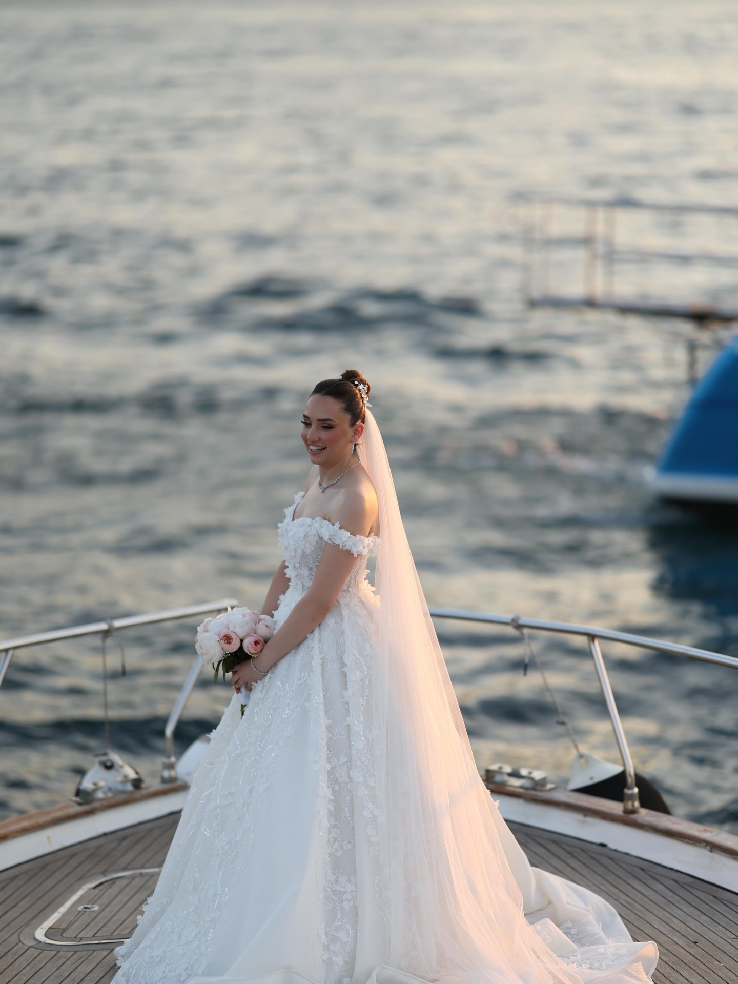 “Ceylan Güres Modaevi prenses siluet gelinlik, uzun duvak ve çiçek detaylı işlemelerle deniz manzarasında çekilmiş gelin pozu”