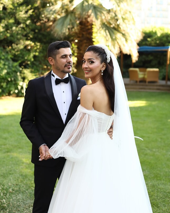 Düşük omuzlu tül kollu A kesim gelinlik ile bahçede çift poz çekimi