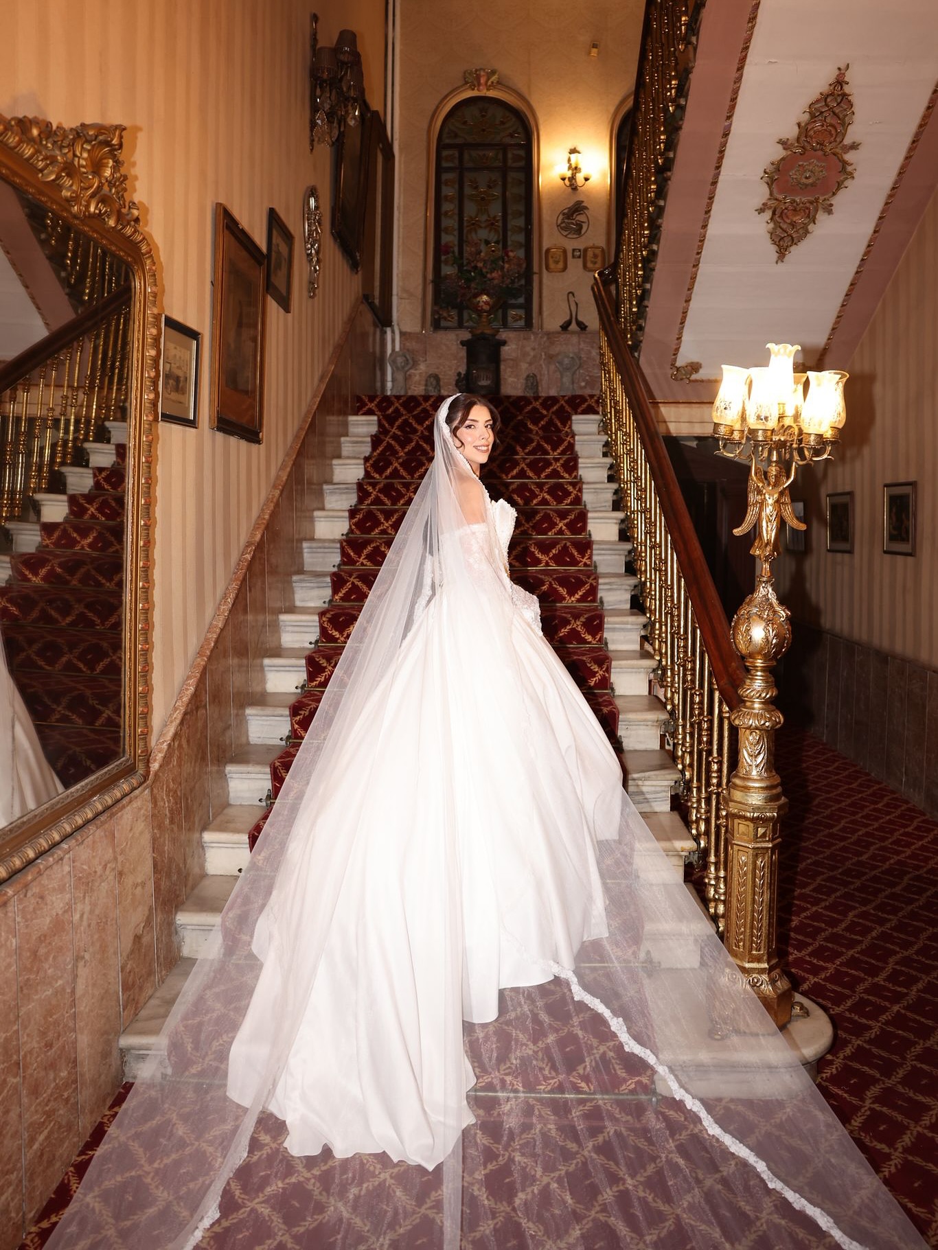 Düşük omuz yaka ve uzun duvak detaylı prenses kesim gelinlik ile merdivenlerde romantik gelin pozu.