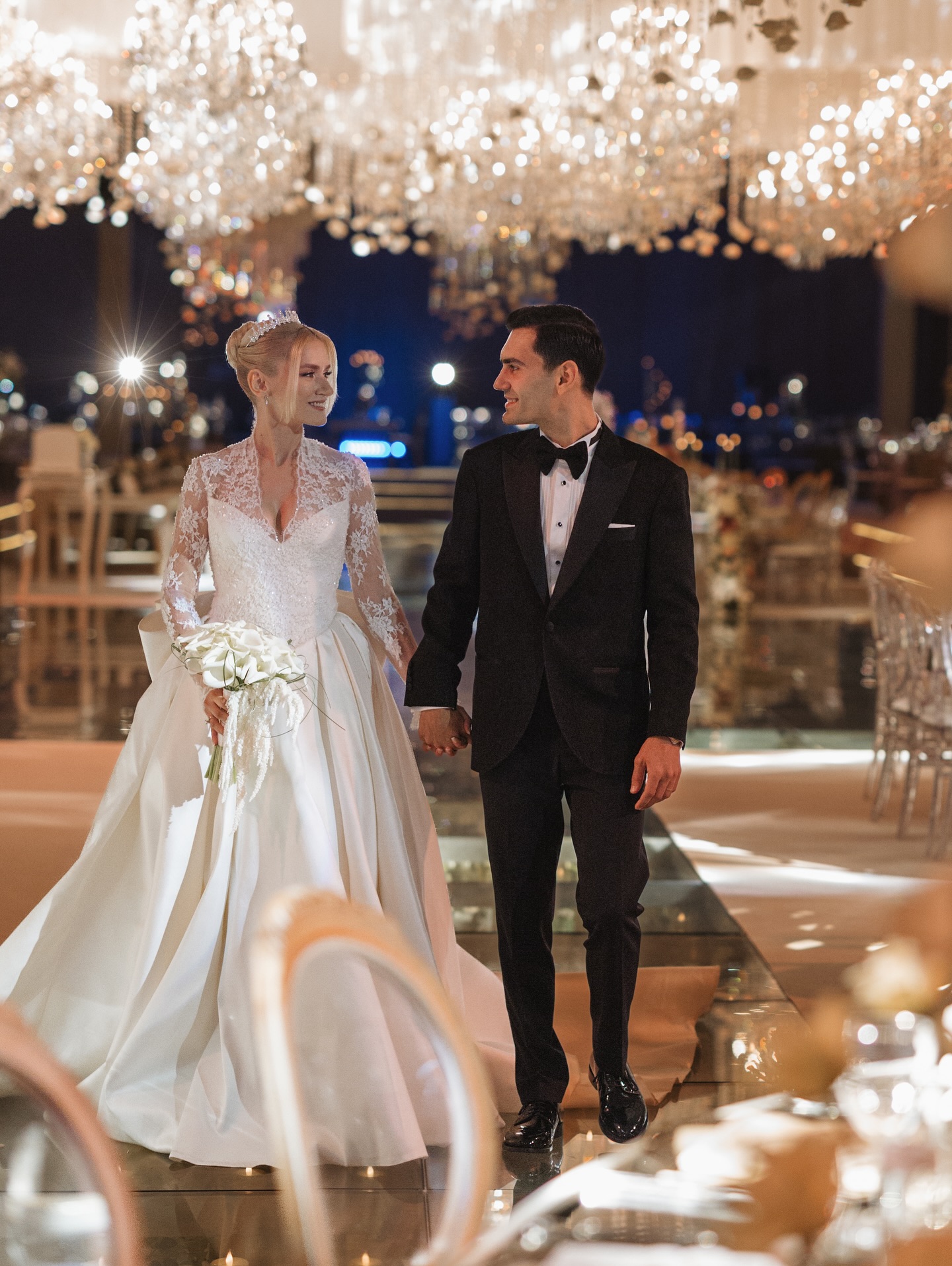 Kristal avizeli düğün salonunda ışıl ışıl ambiyans ve el ele yürüyen çift