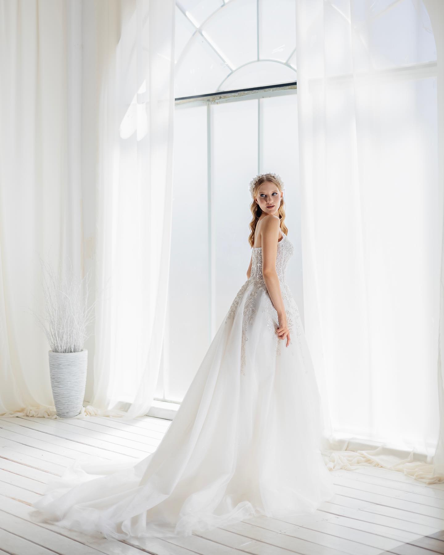 Uzun kollu dantel üstlü A kesim gelinlik, doğal ışıkta pencere önünde