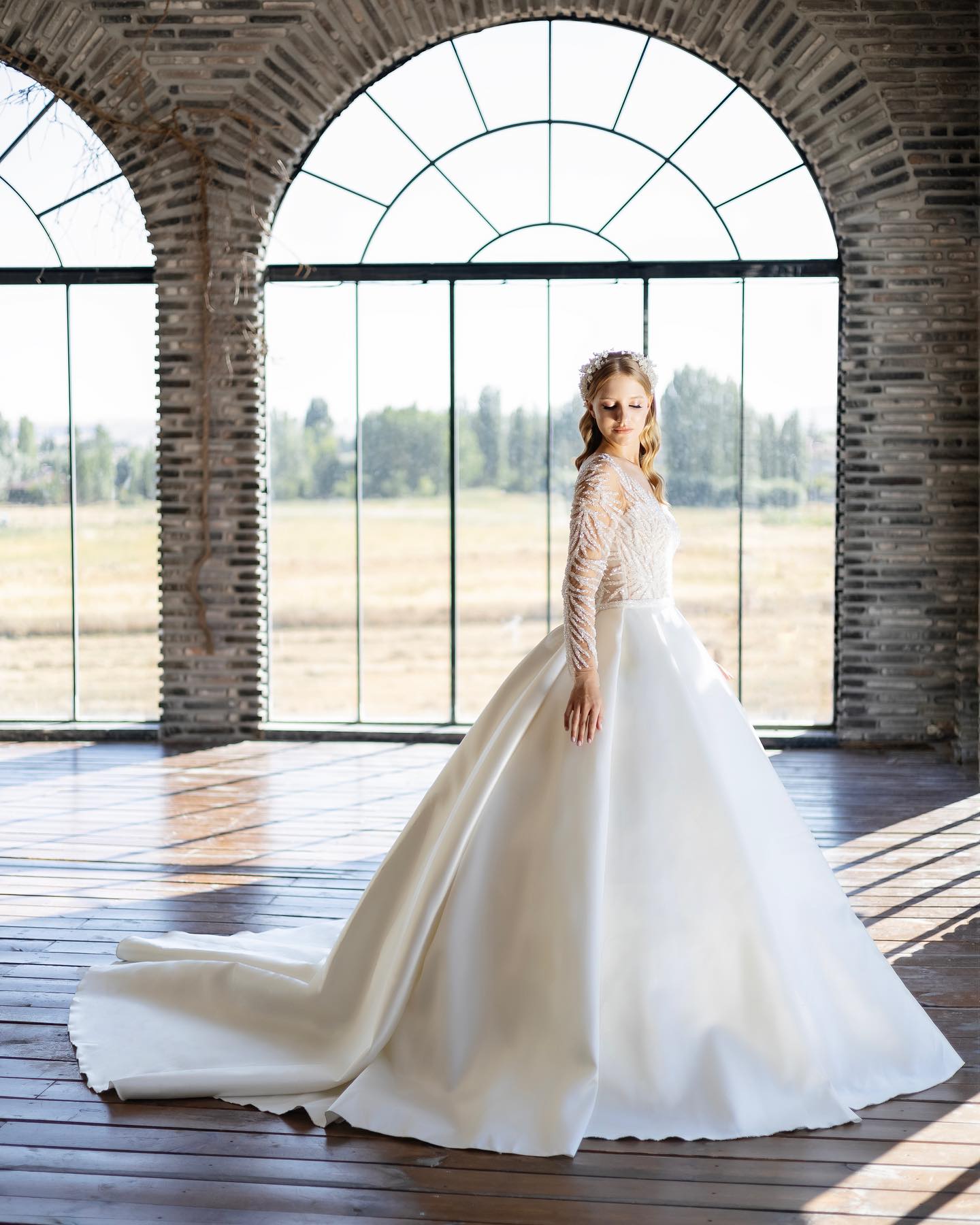 Geniş etekli A kesim gelinlik, kemerli pencere önünde gün ışığı