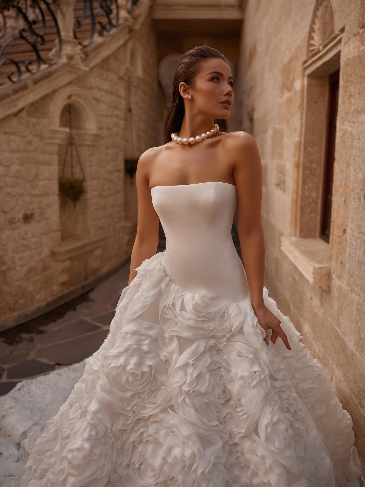 Taş sokakta dış çekimde straplez prenses gelinlik, heykelsi 3D çiçek aplikeleriyle couture etki yaratıyor.