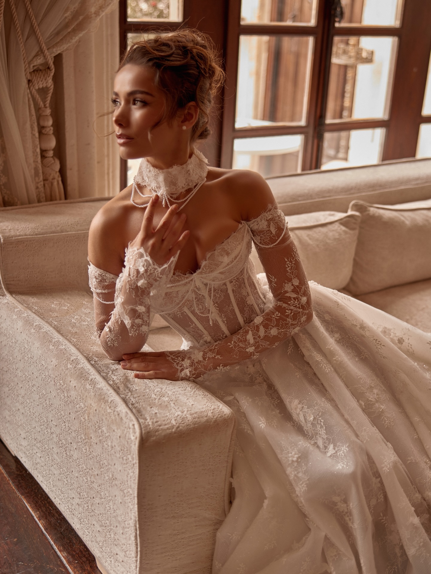 Transparan dantel korse detaylı, A kesim prenses etekli gelinlik ile oturma alanında zarif ve doğal gelin pozu.