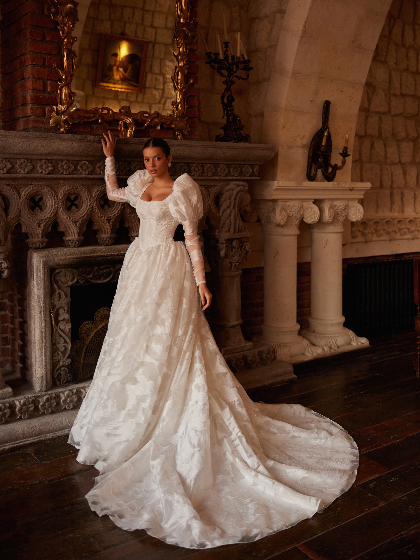 “Tarihi şömine önünde balon kollu gelinlik, uzun kuyruk ve romantik siluet.”