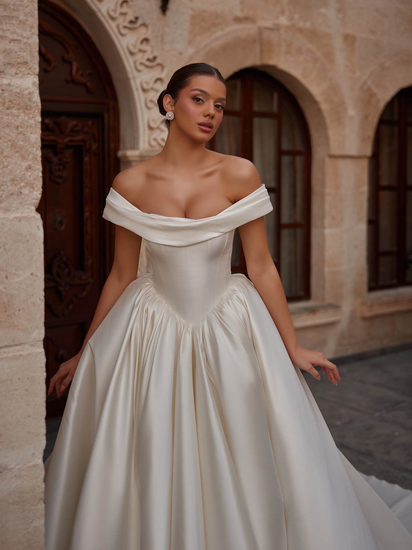 Düşük omuz yaka ve korsaj detaylı saten prenses gelinlik, minimal ve lüks görünüm.