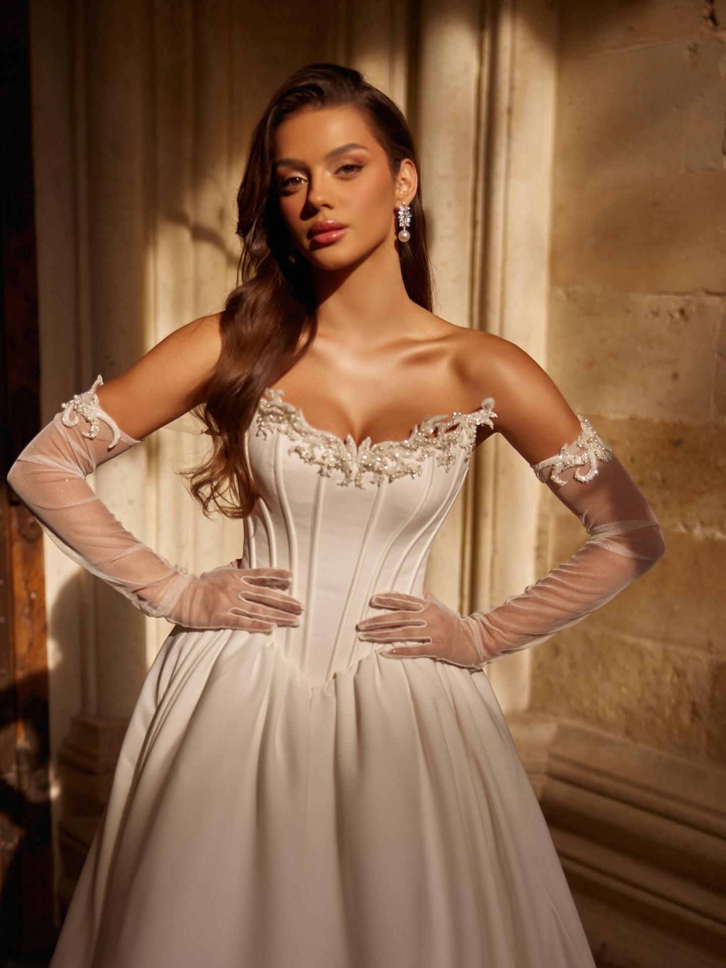 Düşük omuzlu, korse detaylı prenses gelinlik modeli; ışıltılı işlemeli yaka ve tül eldivenlerle romantik ve zarif bir bridal görünüm.