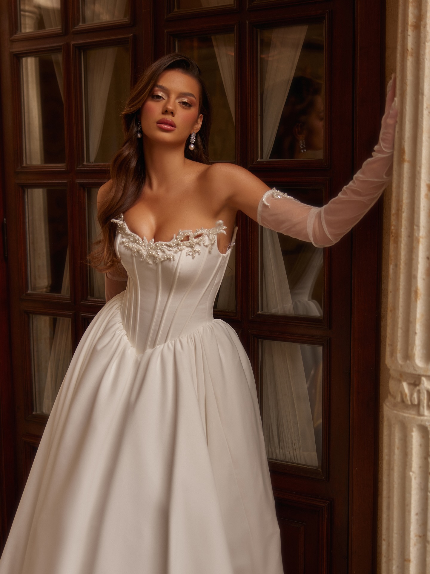 Korse detaylı düşük omuz prenses gelinlik; romantik işlemeli yaka, hacimli etek ve tül eldivenlerle klasik ve iddialı gelin görünümü.