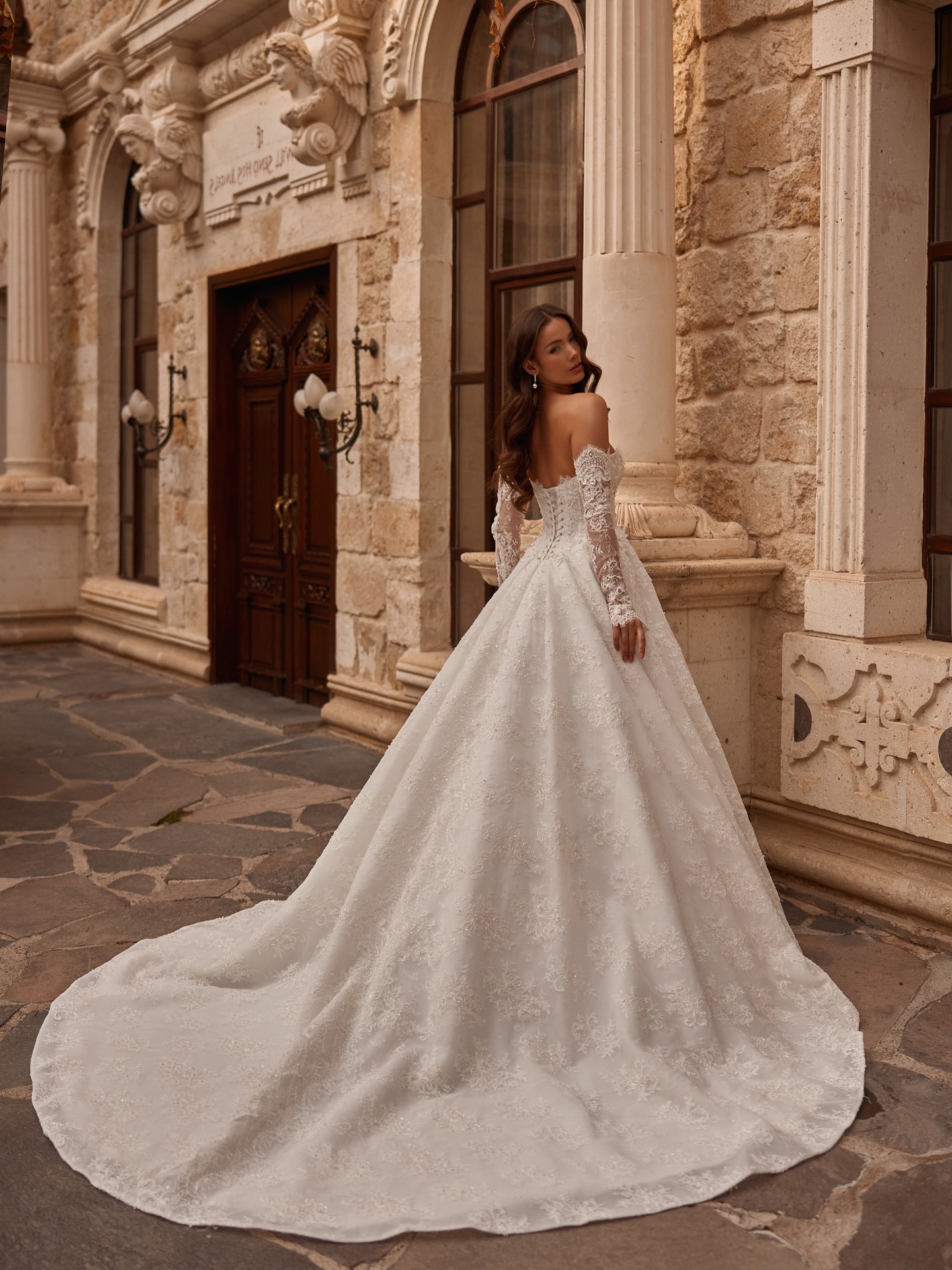  Uzun kuyruklu prenses siluet gelinlik modeli, tarihi taş mimari fon önünde arkadan görünüm.