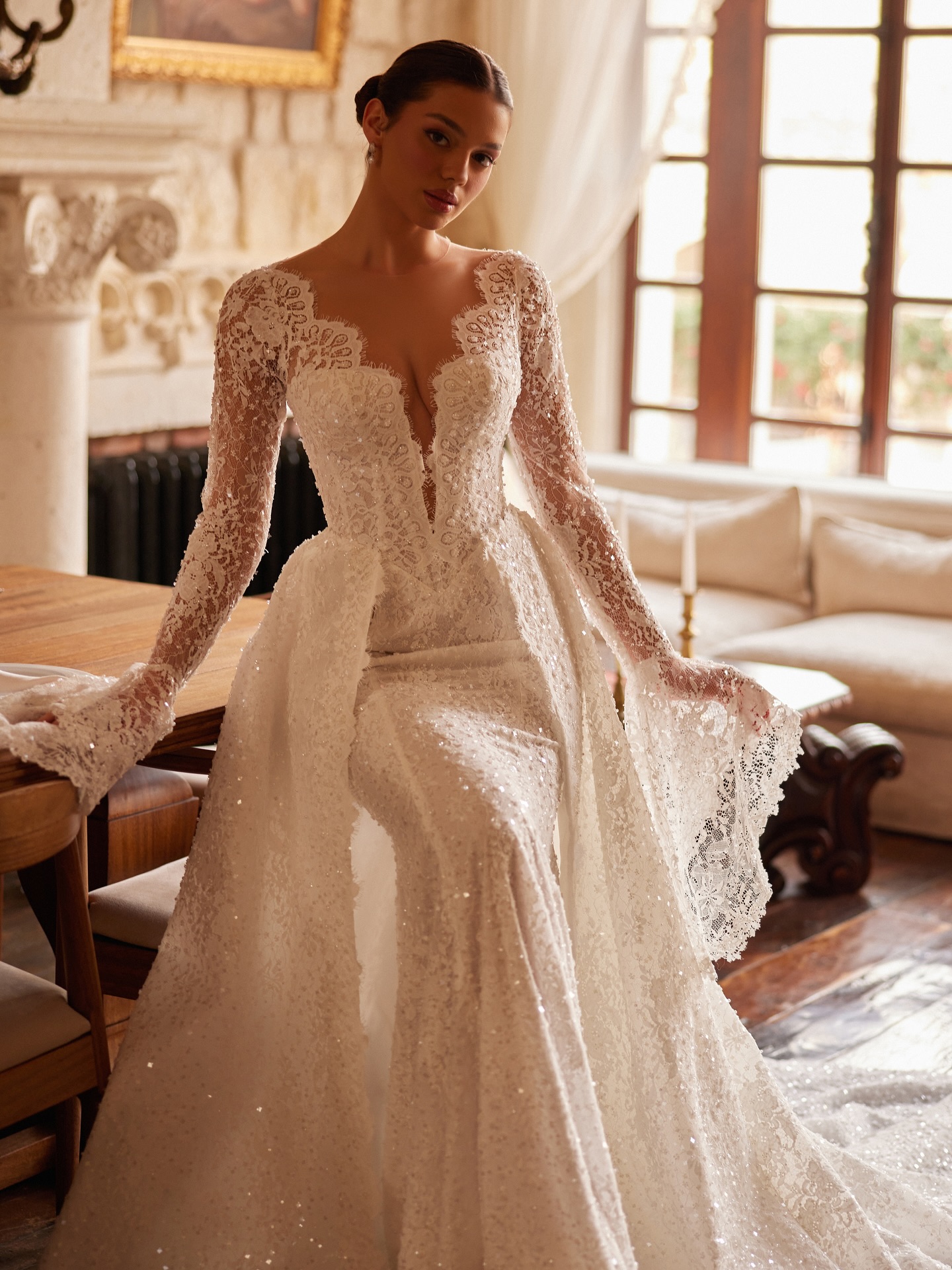 Uzun kollu dantel gelinlik modeli, derin V yaka ve ışıltılı işlemeli kumaş detaylarıyla romantik ve zarif görünüm.