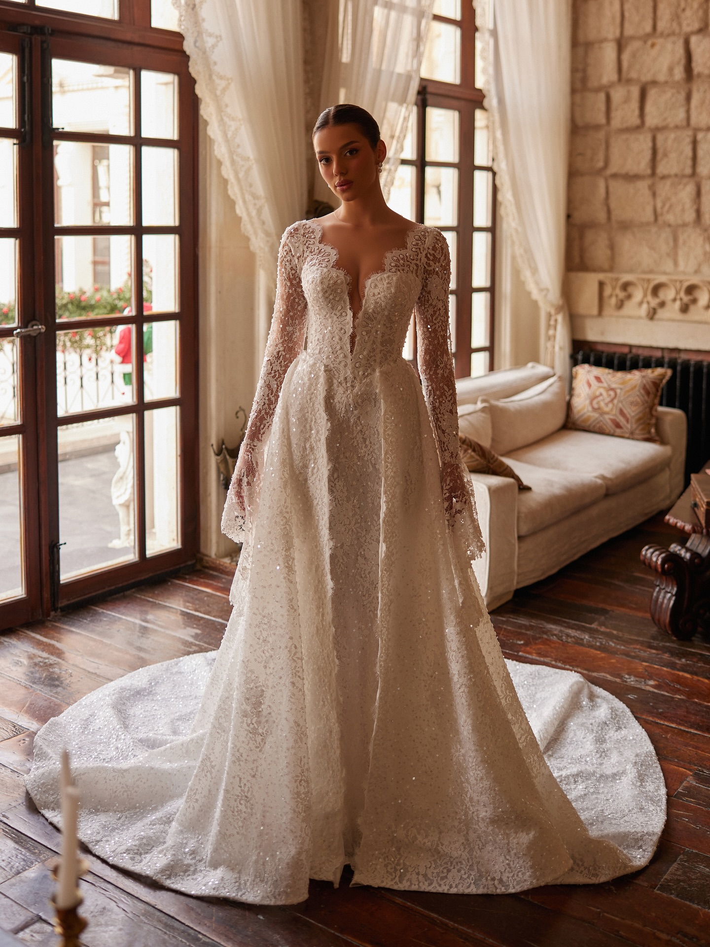 Önden tam boy çekimde dantel işlemeli gelinlik, uzun kol ve ışıltılı doku ile sofistike gelin stili.