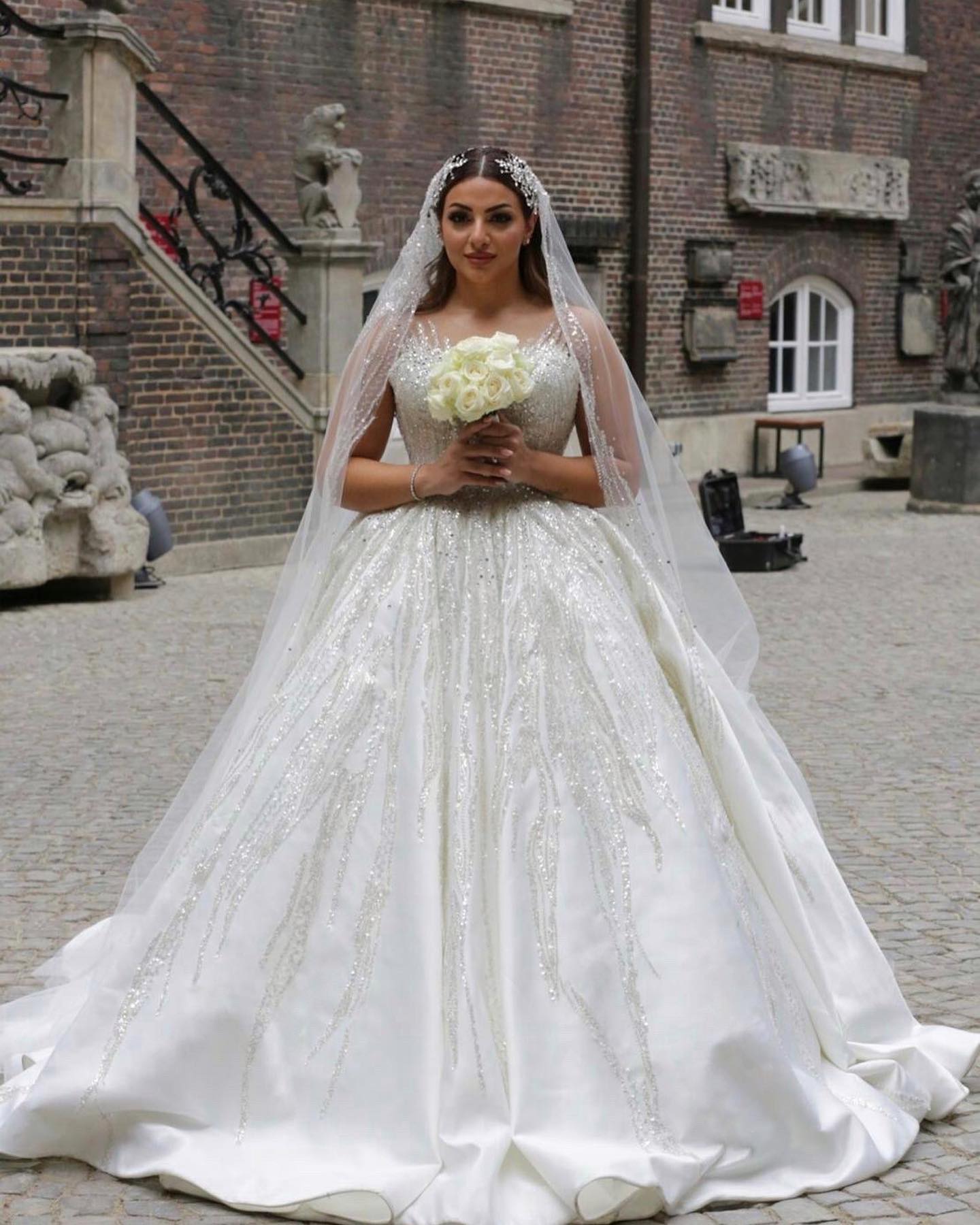 Tam boy prenses gelinlik görünümü, taş işlemeli gövde ve parlak etek desenleriyle dış mekanda poz