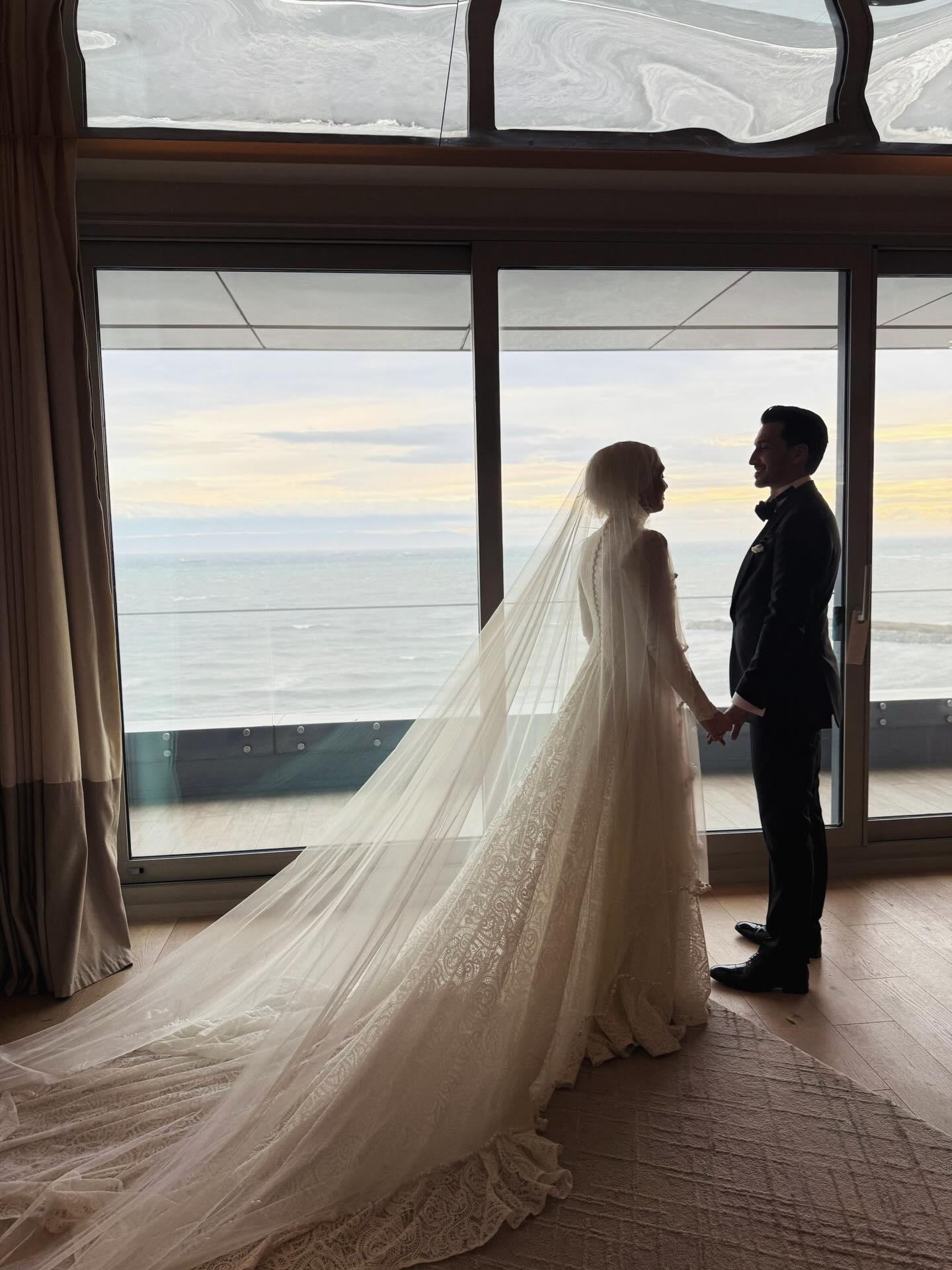 “Özem Keskin tesettür gelinlik ve damat, deniz manzaralı pencere önünde romantik düğün fotoğrafı”