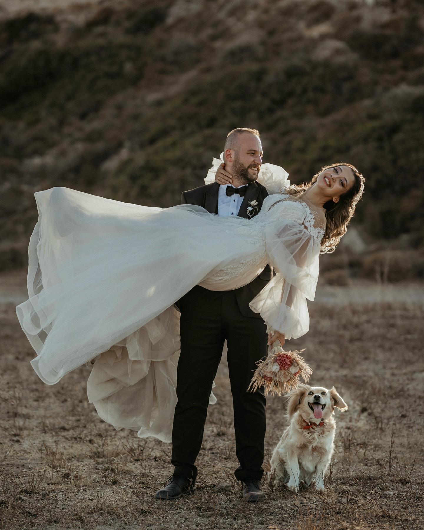 Damat gelini kucağında taşırken A kesim tül gelinlik ve doğal buketle eğlenceli düğün çekimi