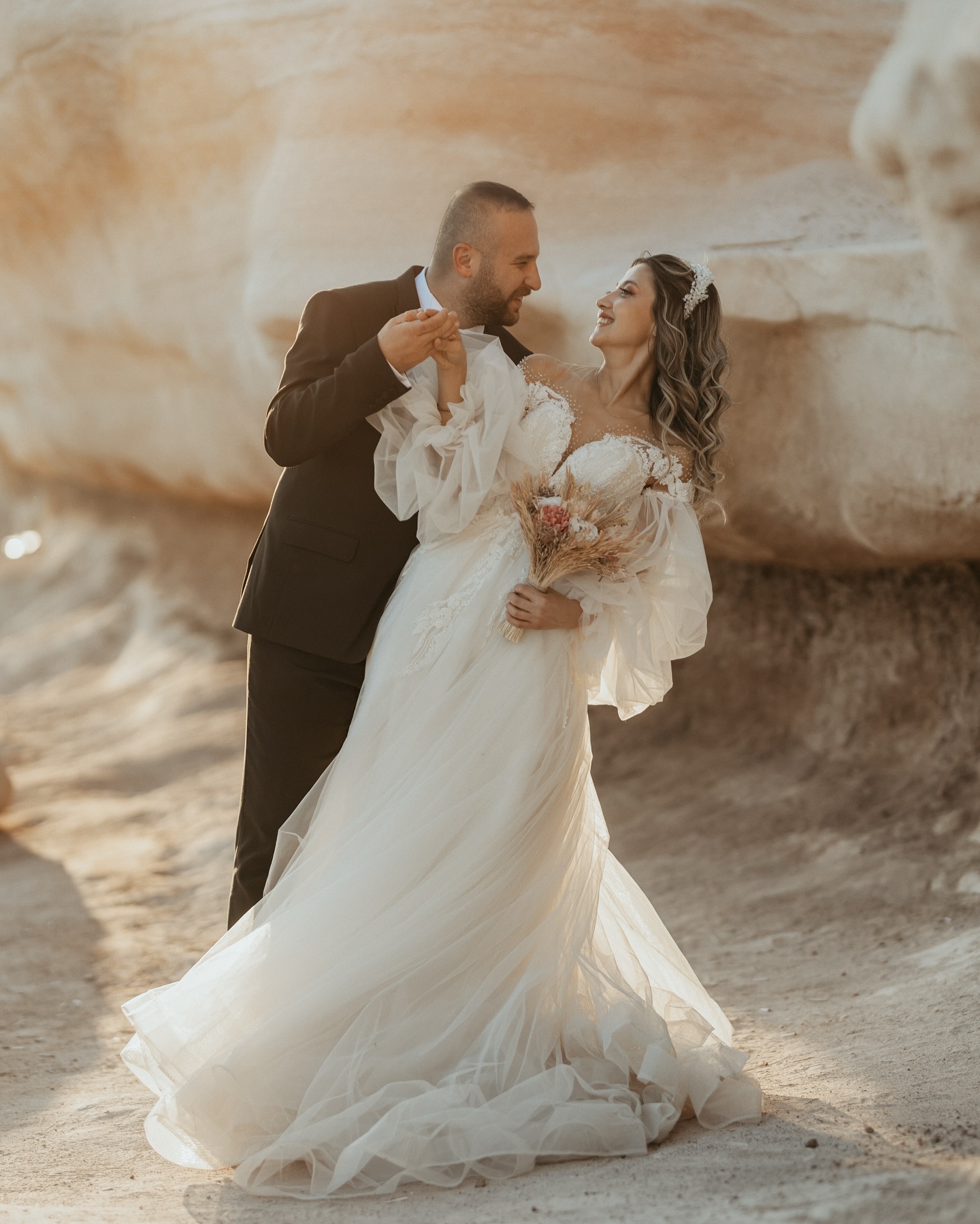 Taş dokulu arka planda A kesim gelinlik ve tül kollarla romantik çift fotoğrafı