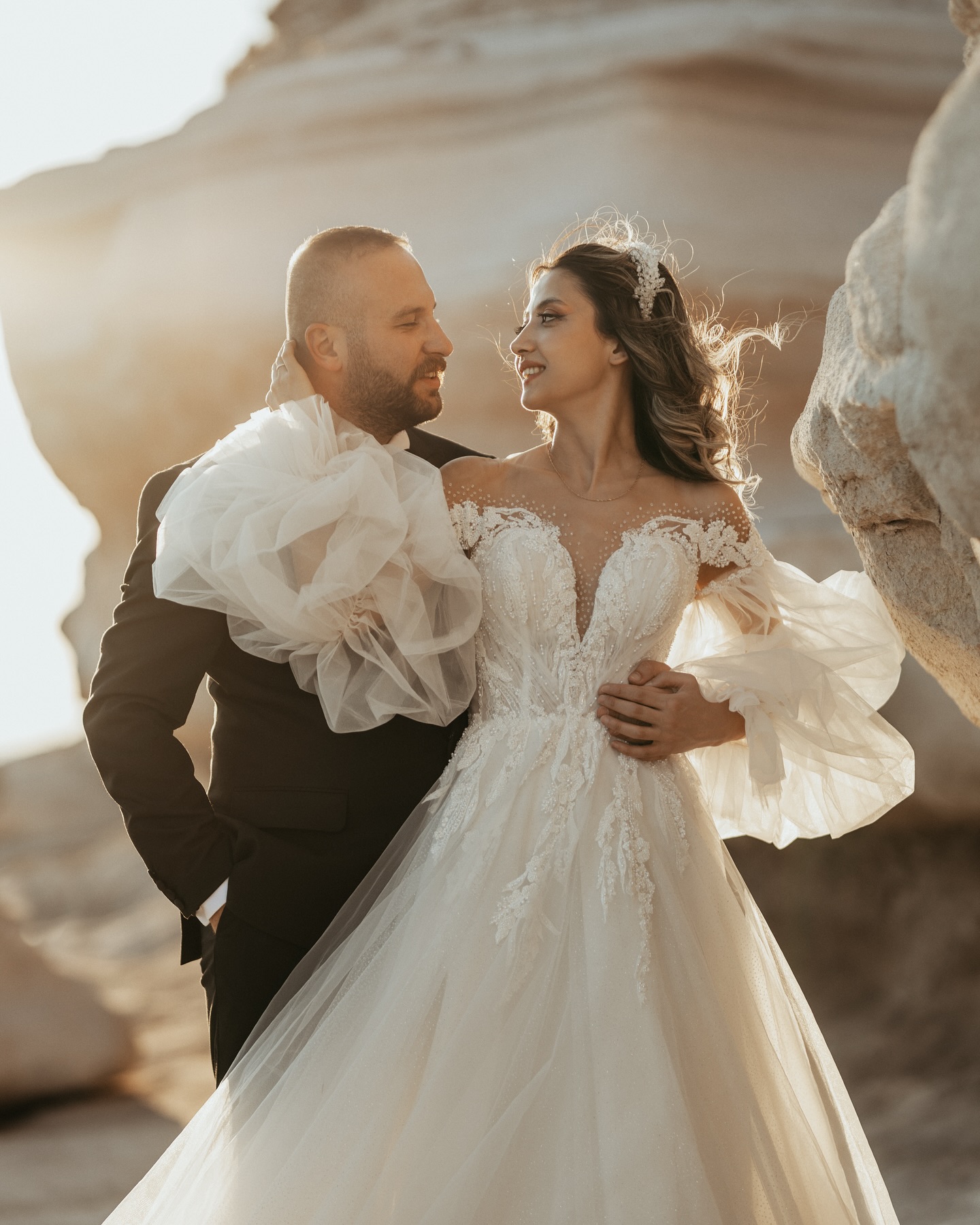 Gün batımında çift pozunda dantel detaylı A kesim gelinlik ve transparan yaka görünümü