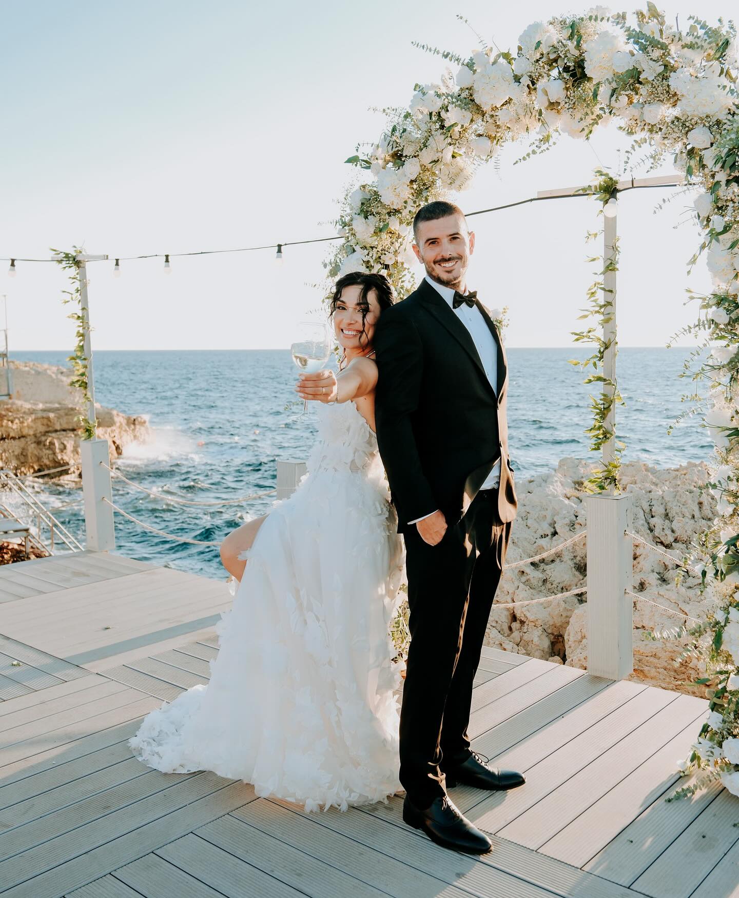 Deniz manzarası önünde çiçek kemer altında straplez 3D çiçek detaylı A kesim gelinlik poz veren gelin