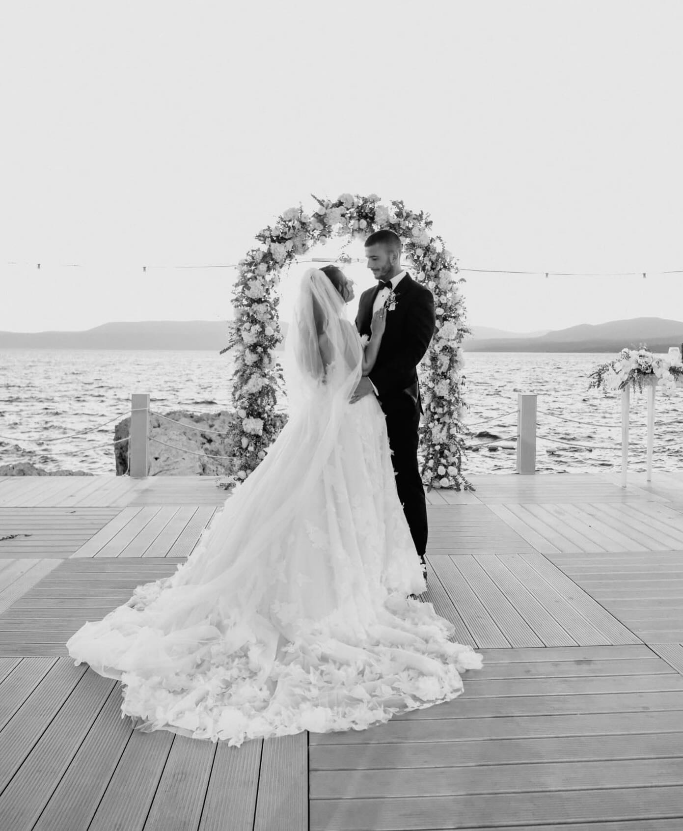 Çiçek kemer önünde uzun duvaklı straplez A kesim gelinlik ile romantik nikah pozu (siyah beyaz)