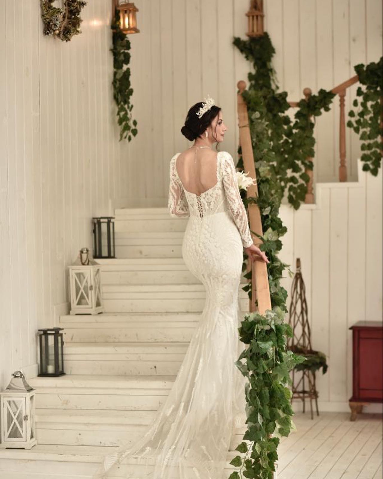 Dantel balık gelinlik, derin sırt dekoltesi ve uzun kollu zarif tasarım – stüdyo merdivenlerinde arka görünüm