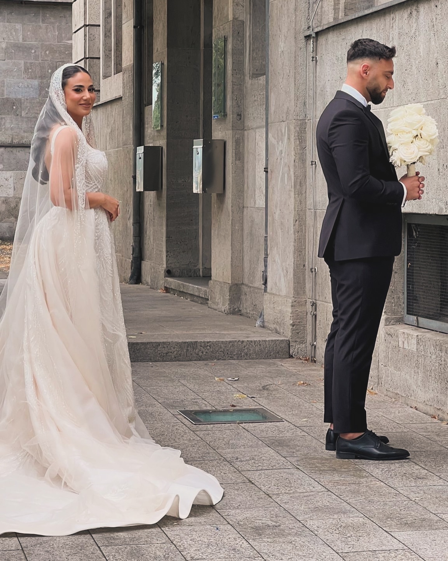 “Işıltılı işlemeli prenses gelinlik ve uzun duvakla romantik dış çekim anı, gelin arkadan yaklaşırken.”