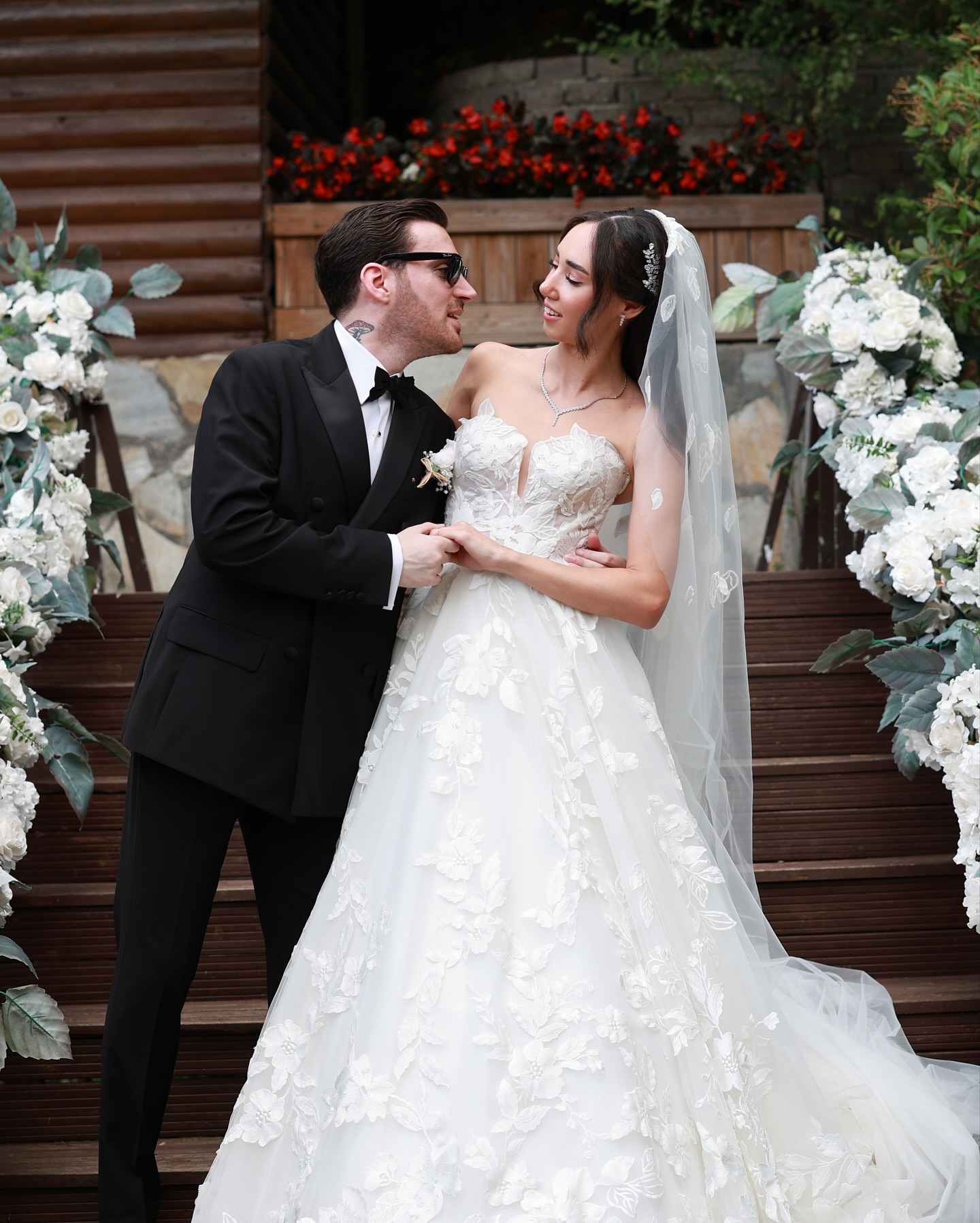 Çiçek dekorları arasında damadın gelini belinden tuttuğu, kalp yaka A kesim gelinliğin detaylarının göründüğü düğün fotoğrafı