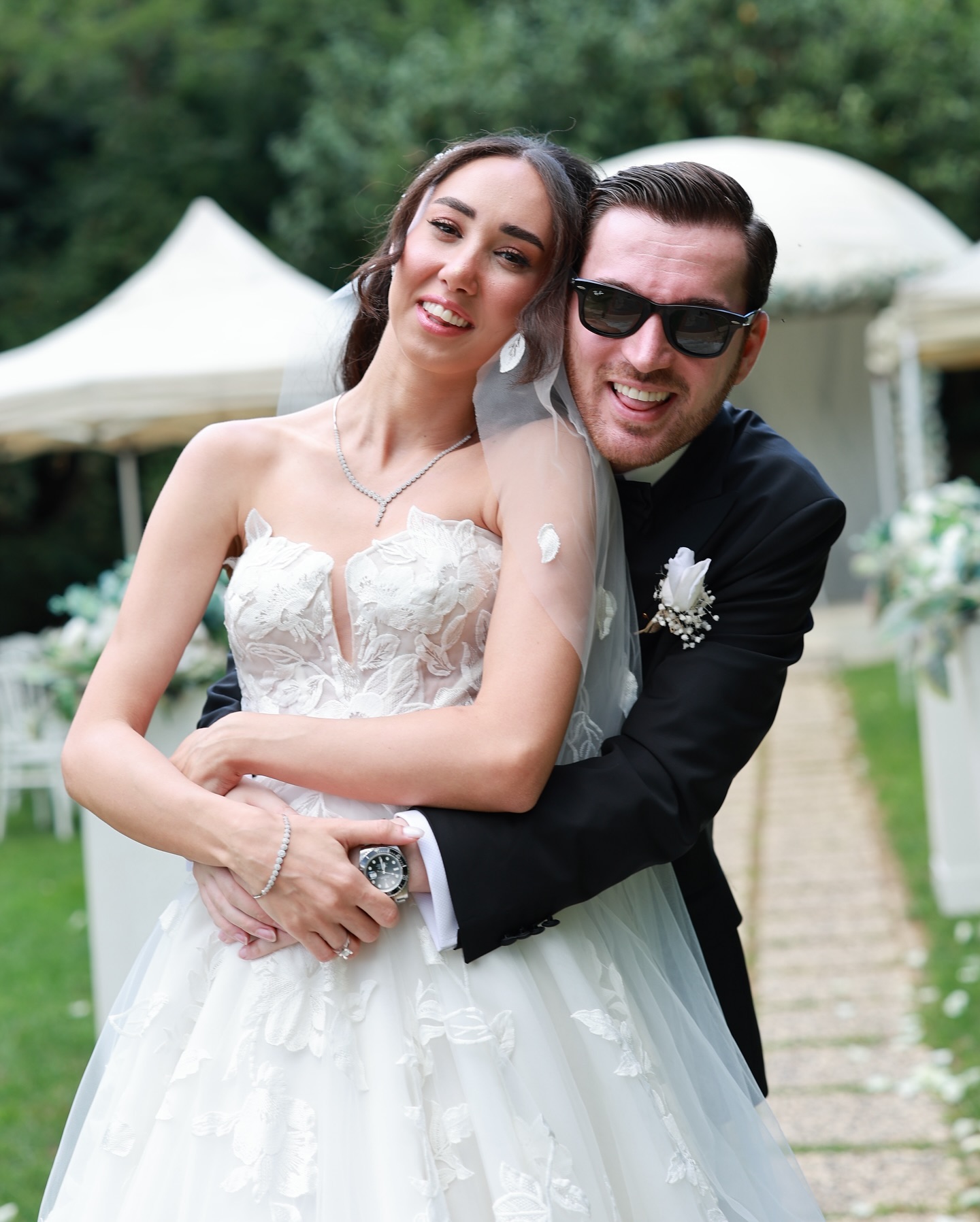  Gelinin çiçek işlemeli A kesim gelinliğiyle damadın arkasından sarıldığı, doğal ve eğlenceli düğün dış çekim fotoğrafı.