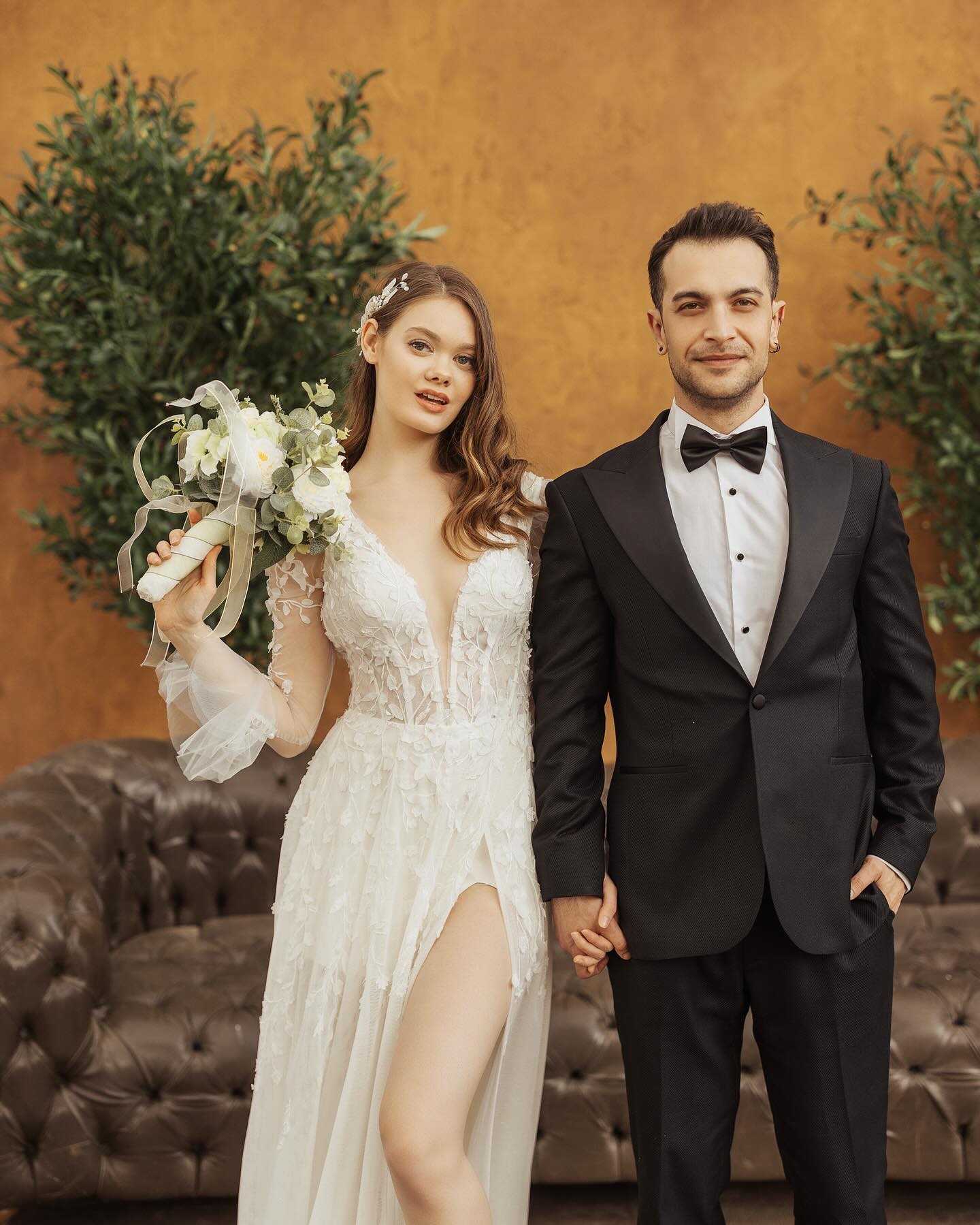 Transparan kollu, çiçek aplikeli ve derin V yakalı gelinlik ile gelin ve damadın yakın plan poz çekimi.